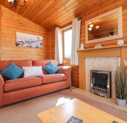 A living room with a red sofa and blue cushions next to a fireplace and a window at Seascape Retreat in Ilfracombe