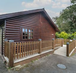 Exterior view of a wooden cabin with a fenced ramp and trees in the background at Ash in Swanage