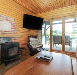 A wooden interior living room with a wood-burning stove a leather armchair a television and glass doors leading to an outdoor seating area at Ash in Swanage
