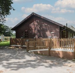 A wooden cabin with a fenced deck and trees around it at Ash in Swanage