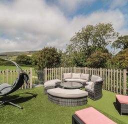 An outdoor seating area with cushioned wicker furniture and hanging chair on artificial grass next to a wooden fence at Ash in Swanage
