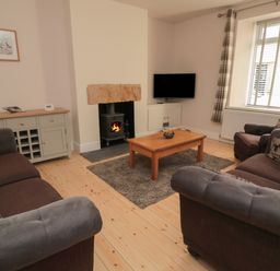 A living room with sofas a wooden coffee table a wood burner and a television at 55 Wellwood Street in Amble
