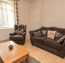 A living room with a brown sofa and armchair with patterned cushions next to a wooden coffee table at 55 Wellwood Street in Amble