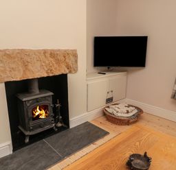 A living room with a wood burning stove fireplace a mounted television a wicker basket with blankets and a wooden coffee table at 55 Wellwood Street in Amble