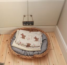 A dog bed with blankets on a wooden floor under a cabinet with a sign at 55 Wellwood Street in Amble