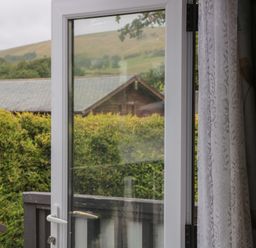 An open glass door with white frame showing a hedge and rooftops outside with hills in the background at Beech in Swanage