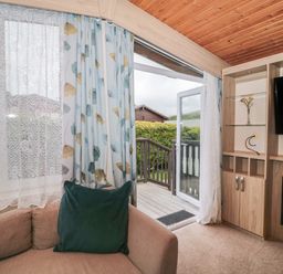 A living room with a beige sofa a green cushion curtains and a glass door leading to a wooden deck at Beech in Swanage