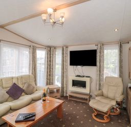 A living room with a leather sofa and armchair a wooden coffee table a wall-mounted TV and a fireplace at Birch in Swanage