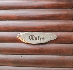 A wooden log cabin wall with a wooden sign reading Oaks at Oaks Swanage