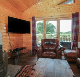 A wooden living room with leather armchairs a wooden table a wall-mounted television and glass doors at Oaks in Swanage