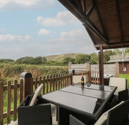 A covered outdoor patio with a glass table and four chairs overlooking fields and hills at Oaks Swanage