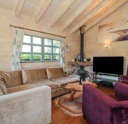 A living room with a large sofa a wooden coffee table two purple armchairs a fireplace and a television at Cherry in Swanage