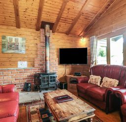 A living room with wooden walls and ceiling a brick wood stove red leather sofas a wooden coffee table and a wall mounted television at Walnut in Swanage