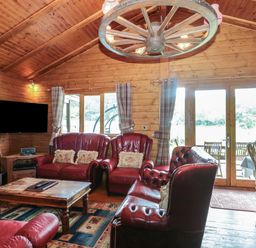 A wooden living room with red leather sofas a wooden coffee table a television and large glass doors at Walnut in Swanage