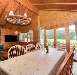A wooden dining room with a table and chairs next to large windows overlooking a garden at Walnut in Swanage
