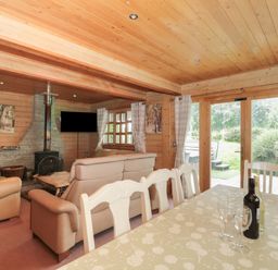 A wooden living room with beige sofas a fireplace a dining table with chairs and glass doors leading outside at Pine in Swanage