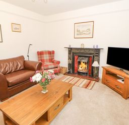 A living room with a brown leather sofa a red plaid armchair a wooden coffee table with flowers a fireplace and a television on a wooden stand at Crookham Dairy Crookham near Etal