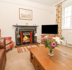 A living room with a fireplace a television a wooden coffee table with flowers and armchairs at Crookham Dairy Crookham near Etal