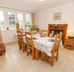 A dining room with a wooden table set for six people with a fireplace and a plaid sofa at Crookham Dairy Crookham near Etal