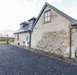 An exterior view of a stone and stucco house with gravel driveway at The Artist's Barn in Ayle near Cappawhite