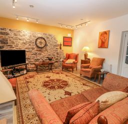 A living room with two armchairs a sofa a rug a television and a stone accent wall at The Artist's Barn in Ayle near Cappawhite