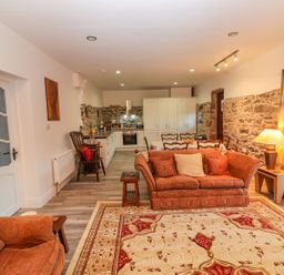 An open living room and kitchen with stone walls a patterned rug and upholstered furniture at The Artist's Barn Ayle near Cappawhite