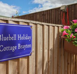 A sign for Bluebell Holiday Cottage Brayton attached to a wooden fence