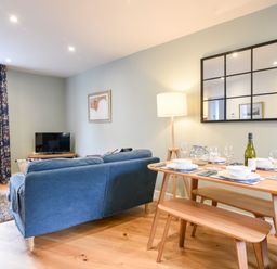 A living room with a blue couch a wooden dining table set with dishes and glasses and a floor lamp at Conybeare Cottage in Lyme Regis