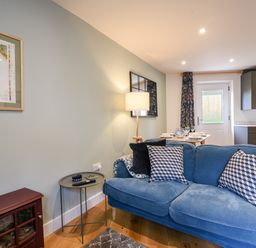 A living room with a blue sofa pillows a side table lamp and dining table in the background at Conybeare Cottage in Lyme Regis