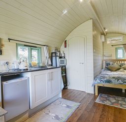 A compact kitchen and bedroom inside a wooden cabin with white cabinets and a bed at Pendragon Pod in Axminster