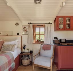 A tiny house interior with a bed, chair, and kitchen at Spindleberry Hut in Piddletrenthide
