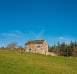 A stone house on a grassy hill with trees in the background at The Hidden Place in Watermillock near Pooley Bridge