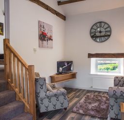 A living room with patterned armchairs a wall clock a small window and a television at The Hidden Place in Watermillock near Pooley Bridge