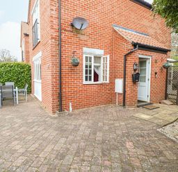 A brick house exterior with a white door open and a window open patio furniture and greenery at 30 Burtons Mill in Stalham