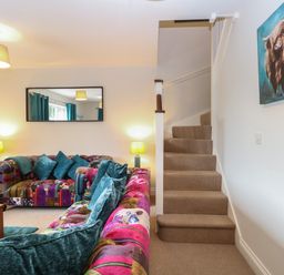 A living room with patchwork sofas and teal cushions next to carpeted stairs at 30 Burtons Mill in Stalham