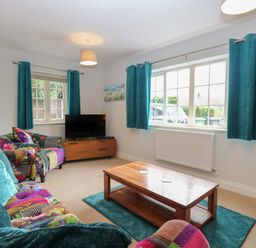 A living room with a wooden coffee table teal curtains and a colorful sofa at 30 Burtons Mill in Stalham