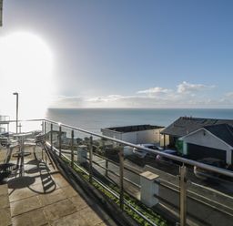A balcony with a table and chairs overlooking the sea and neighboring houses at Looe Island View in Downderry