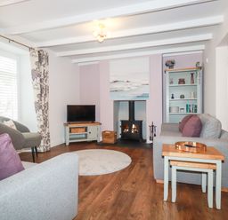 A living room with gray sofas purple cushions a fireplace television and wooden flooring at Still Waters in Pentewan