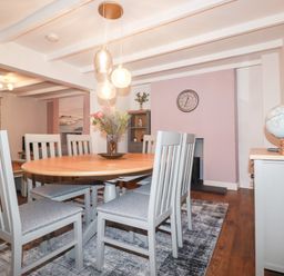A dining room with six chairs around a wooden table a vase with flowers pendant lights a clock a globe and a cabinet at Still Waters in Pentewan