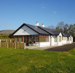 A single story white house with a dark roof and fenced patio on a lawn at Rose Cottage in Muff County Donegal