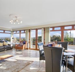 A living room with leather sofas chairs a dining table and large windows at Rose Cottage in Muff County Donegal
