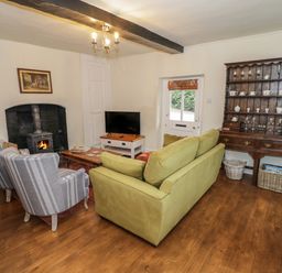 A living room with a wood burning stove two armchairs a green sofa a wooden cabinet and a television at Grove Cottage in Leominster