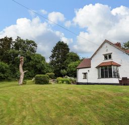 A white detached house with a lawn and trees at Grove Cottage in Leominster