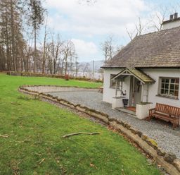 A cottage with a gravel path and wooden bench surrounded by grass and trees at Larch Cottage at Esthwaite Water in Hawkshead