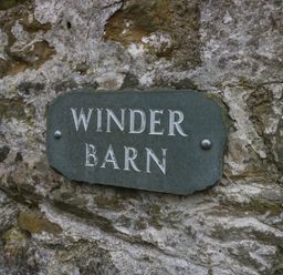 A weathered stone wall with a sign reading Winder Barn at Winder Barn in Askham Cumbria