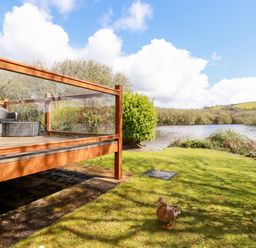A glass-railed wooden deck with outdoor furniture near a lake with a duck on the grass at Lake View 10 in Par