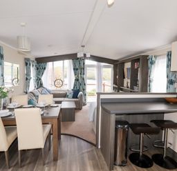 A dining area with table and chairs next to a kitchen counter with stools and a living room with sofa and curtains at Lake View 10 in Par
