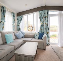 A living room with a gray sectional sofa and a wooden coffee table next to large windows with blue patterned curtains at Lake View 10 in Par