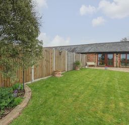 A garden with a tree lawn plants flower pots and a brick building with large windows at Bee Happy Barn in Beighton near Acle
