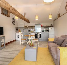 An open plan living area with a sofa a coffee table a dining table and chairs a kitchen with appliances and exposed wooden beams at Bee Happy Barn in Beighton near Acle